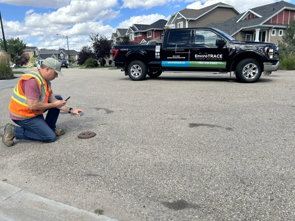 Worker inspecting manhole cover, vehicle in background.