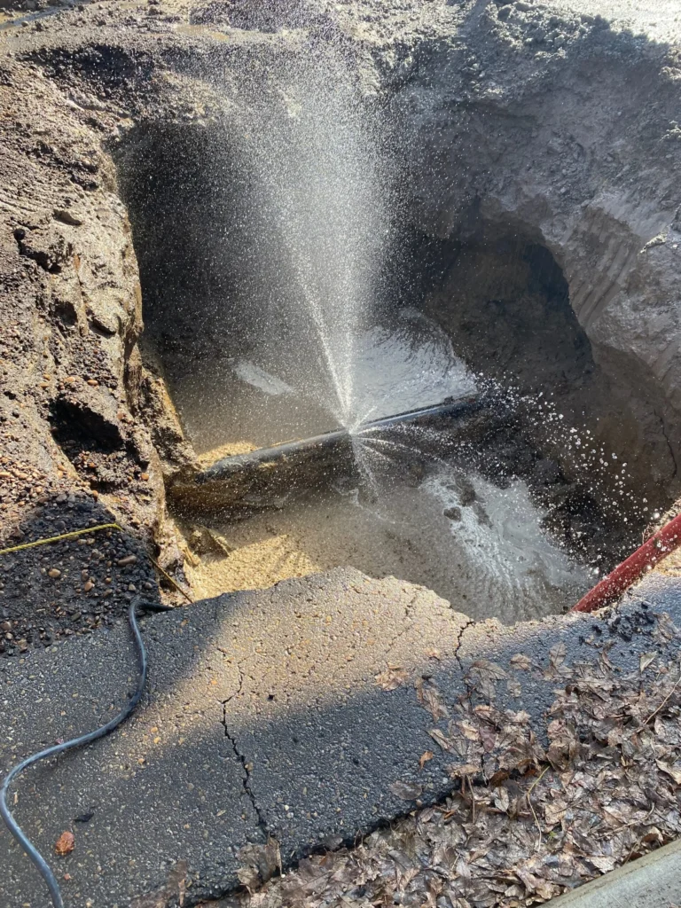 Burst water pipe in large muddy excavation site.